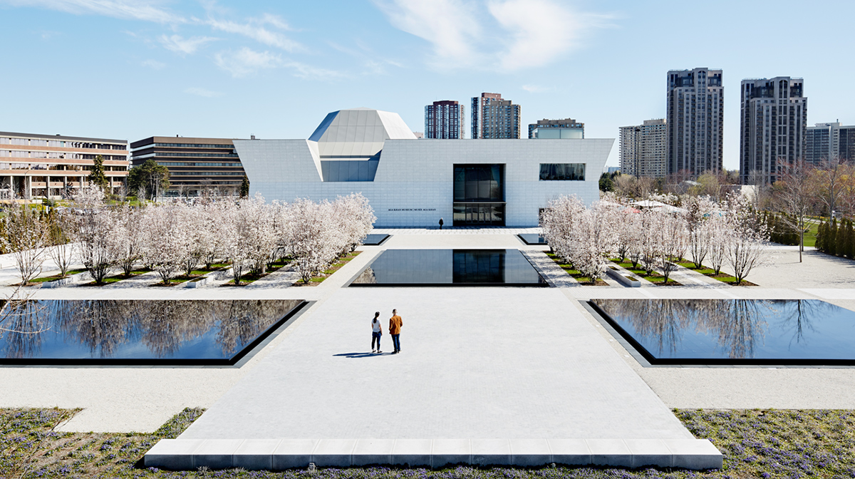 Two people stand in the middle of the Aga Khan Park in Toronto facing the west facade of the Aga Khan Museum.